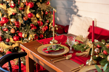 Festive table setting for Christmas dinner at home. Holiday Served table with decorations, candles and garland. Beautiful table setting with Christmas decorations and dishware in living room. 