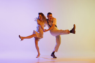 Beautiful girl and man in retro style costumes dancing incendiary dances isolated on gradient lilac...