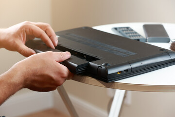 Repairman's hands removing the power battery from the laptop. Computer service and repair concept....