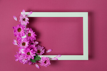 White photo frame decorated with purple chrysanthemum flowers on violet background. Floral composition. Template, top view, flat lay.