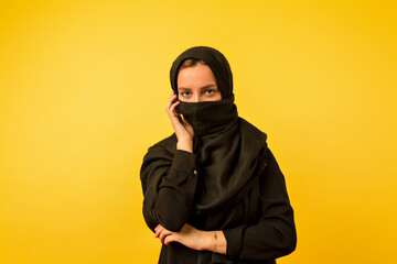 Indoor photo of eastern woman wearing black clothes looking aside with great smile on isolated yellow background