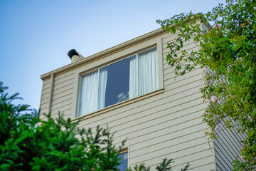 Hidden window in a secret part of the yard or garden with front yard trees with beige slatted exterior with visible windows