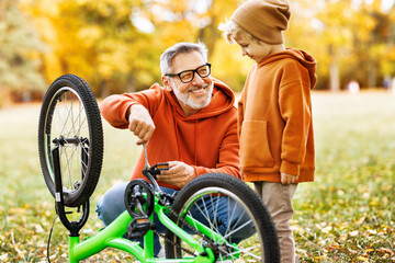 grandfather and grandson repair bicycle outdoors in the autumn park