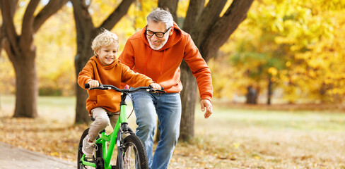 Happy family grandfather teaches child grandson  to ride a bike in park - 550295950