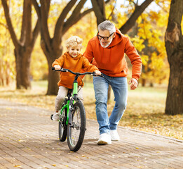 Happy family grandfather teaches child grandson  to ride a bike in park