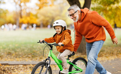 Happy family grandfather teaches child grandson  to ride a bike in park - 550295978
