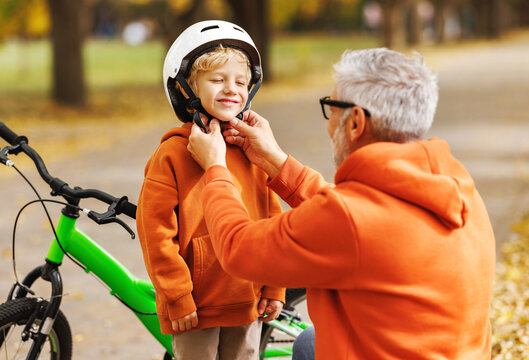 Happy family grandfather puts on grandson helmet for safe cycling in park