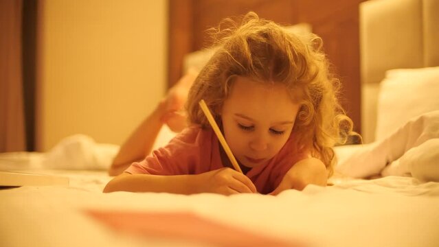 Focused little blonde girl draws or writes something in the bed