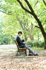 公園でスマートフォンを見る男子高校生