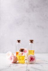 Some bottles with rose essential aroma oil and rose flowers on light  grey textured background. Selective focus. Place for text.