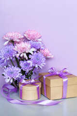 Romantic congratulations to a loved one on birthday, women's day on March 8 or Mother's day. Bouquet of delicate chrysanthemums and two gifts in boxes with purple ribbons on pastel pink background