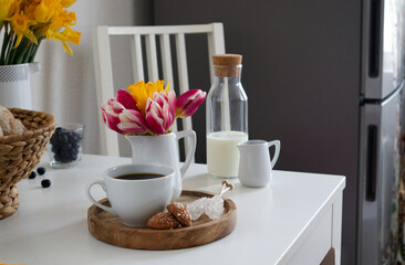 A cup of coffee and a vase with tulips and daffodils on a wooden stand on a table in the kitchen