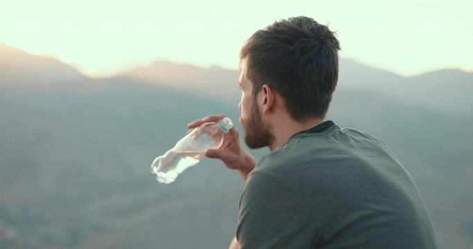 Portrait of an ethnic Caucasian with an inspired bearded face. a young adult thoughtful guy is sitting on top of a mountain, drinking water from a plastic bottle and dreaming, enjoying the sunset rays