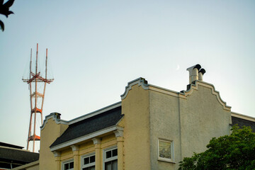 Fototapeta na wymiar Sutro tower in background with a white stucco facade with visible windows and red and blue gradient sky with front yard trees