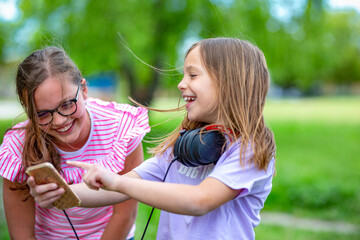 Two young school girls using phone o take selfies and wearing headphones