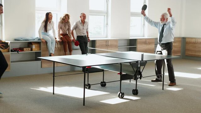 Happy business people are relaxing during work break playing ping pong in office.