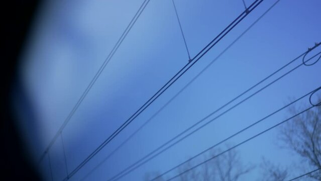 Passenger POV of train window seeing electric wire poles passing by in blue sky
