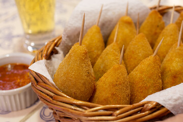Fried chicken coxinhas served in a bar basket with pepper sauce and beer composing