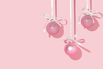 Christmas creative layout with pink Christmas baubles hanging on satin ribbons on pastel pink background. 80s or 90s retro fashion aesthetic concept. Minimal New Year celebration idea with copy space.