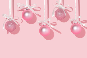 Christmas creative layout with pink Christmas baubles hanging on satin ribbons on pastel pink...