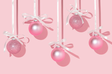 Christmas creative layout with pink Christmas baubles hanging on satin ribbons on pastel pink...