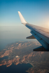 Fototapeta premium Plane window view of clouds and islands surrounded by sea and airplane wing. Traveling concept