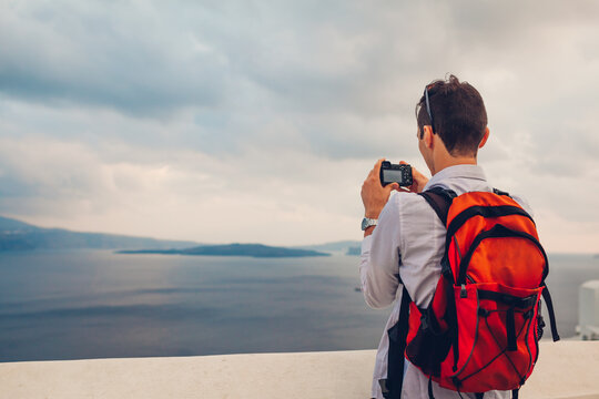 Santorini tourist man taking photo of Caldera sea view from Oia, Greece on camera. Backpacker travels during summer