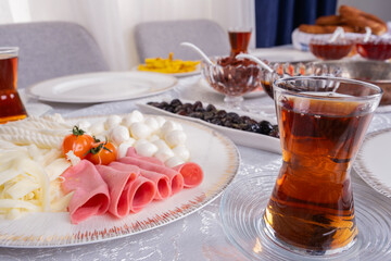 Turkish tea, close up photo glass of fresh hot Turkish tea. Modern breakfast table. Sunday morning family routine. Knit, String and ball of cheese with ham in plate. Ready for eating.