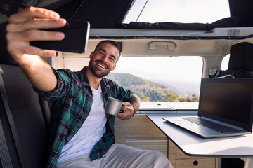 smiling young man taking a selfie inside his camper van using his mobile phone, concept of freedom and digital nomad lifestyle - Powered by Adobe
