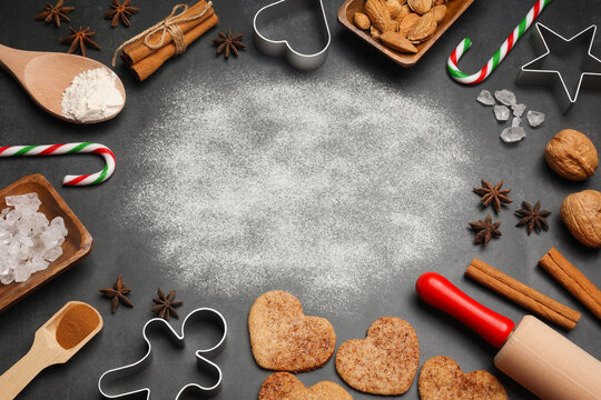 Top view of cinnamon cookies, candy canes, kitchen utensils and spices on dark background. Place for text