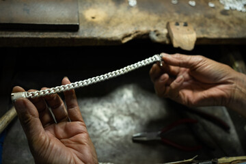 A craftsman is holding a stainless steel bracelet in his hand. At the desk. handmade concept The bracelet is made of real silver.