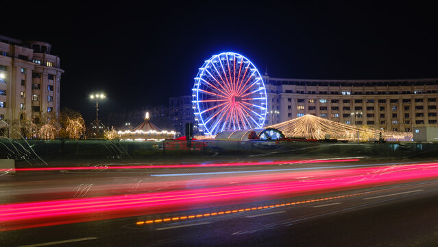 Christmas holiday ferris wheel in Bucharest, Romania, at night, with car light trails.