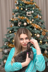 A beautiful Caucasian girl gently holds a plush rabbit in her arms against the backdrop of a Christmas tree.