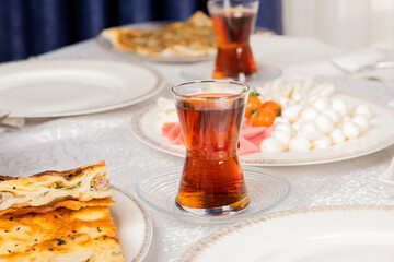 Turkish tea, close up photo of Turkish tea in breakfast table. Traditional morning dish. Patty called su borek with meat. Cheese plate, salami, raw ham on the desk. Family morning routine concept idea