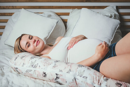 Beautiful pregnant woman relaxing in comfortable bed with pregnancy pillow