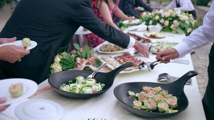 Variety of tasty dish on banquet table, servant in uniform serving invited guests with unique appetizers and snacks. Elegant party outdoor, catering food service