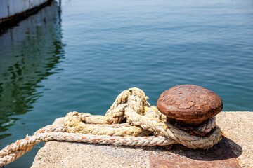 Fototapeta na wymiar Dettaglio di una bitta con un aocrda in un porto di mare