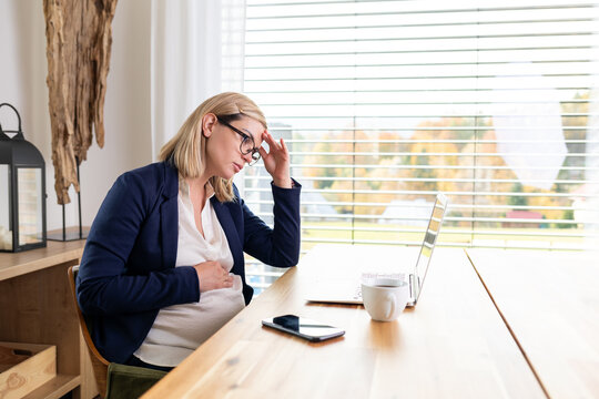 Tired pregnant woman working remotely on laptop at home