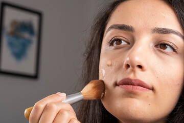 Liquid foundation, woman applying liquid foundation on her face with brush. Close up home perfect...