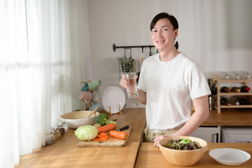 Fototapeta na wymiar An Asian young man drinking fresh water in kitchen at home , healthy lifestyle concept