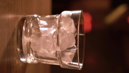glass with ice on a bar counter and bartender mixing cocktail in a shaker on background