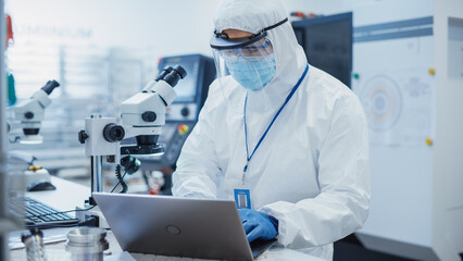 Electronic Manufacturing Factory: Engineer in Sterile Coverall Working on Laptop Computer,...