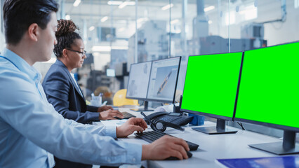 Factory Office: Industrial Engineers Drafting Equipment 3D Layouts of a Heavy Industry Machine Parts on a Computer CAD Software. One Computer Monitor Display is a Green Screen Mock Up Template.