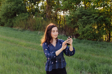 Young woman laughing and typing message in smart phone in the green field