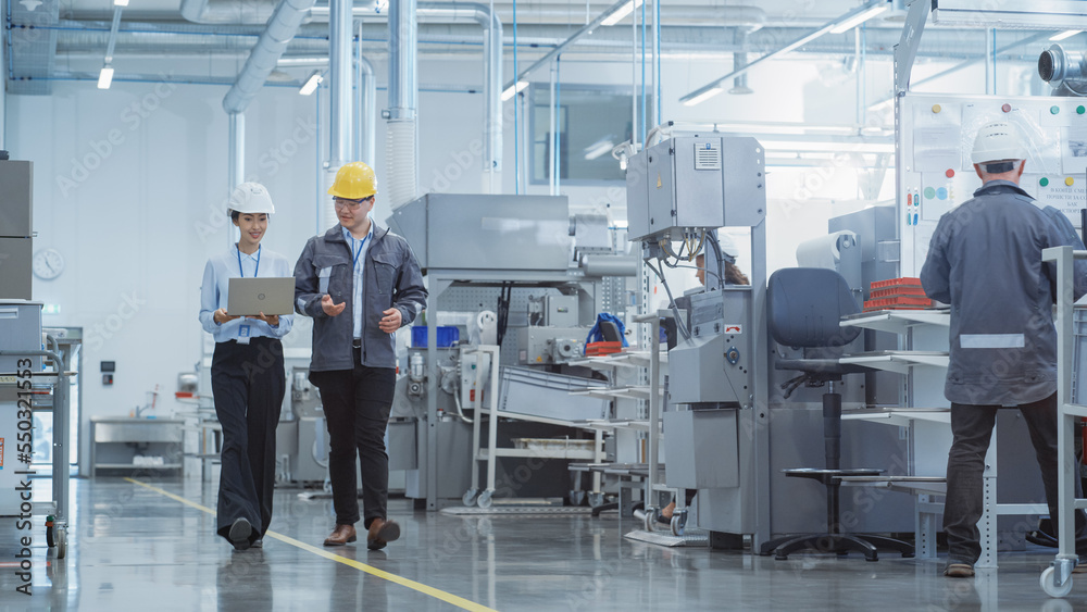 Poster portrait of two young asian heavy industry engineers in hard hats with laptop computer talking in a 