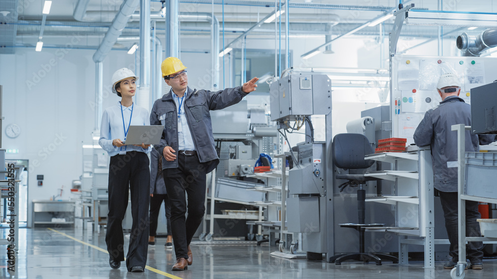 Poster portrait of two young asian heavy industry engineers in hard hats with laptop computer talking in a 