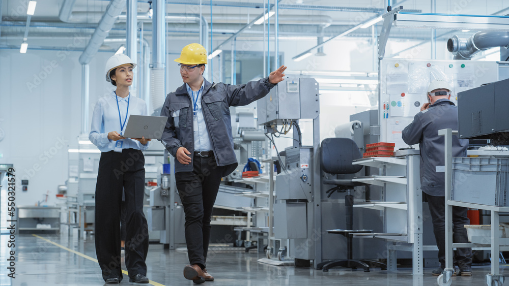 Poster two young asian heavy industry engineers in hard hats walking with laptop computer and talking in a 