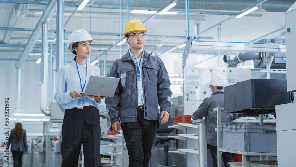 Poster two young asian heavy industry engineers in hard hats walking with laptop computer and discussing wo