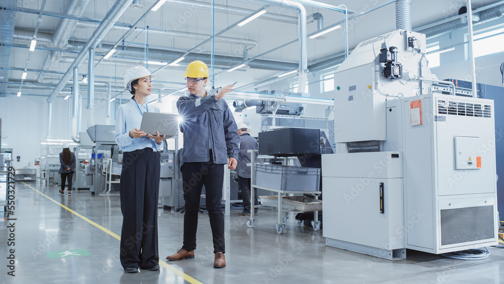 Poster two heavy industry employees in safety uniform and hard hats walking and talking in a factory. asian