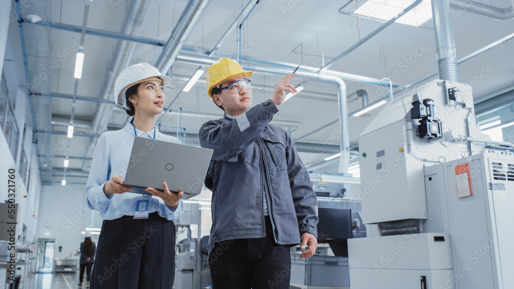 Leinwandbilder two heavy industry employees in hard hats discussing job assignments at the factory, using laptop co
